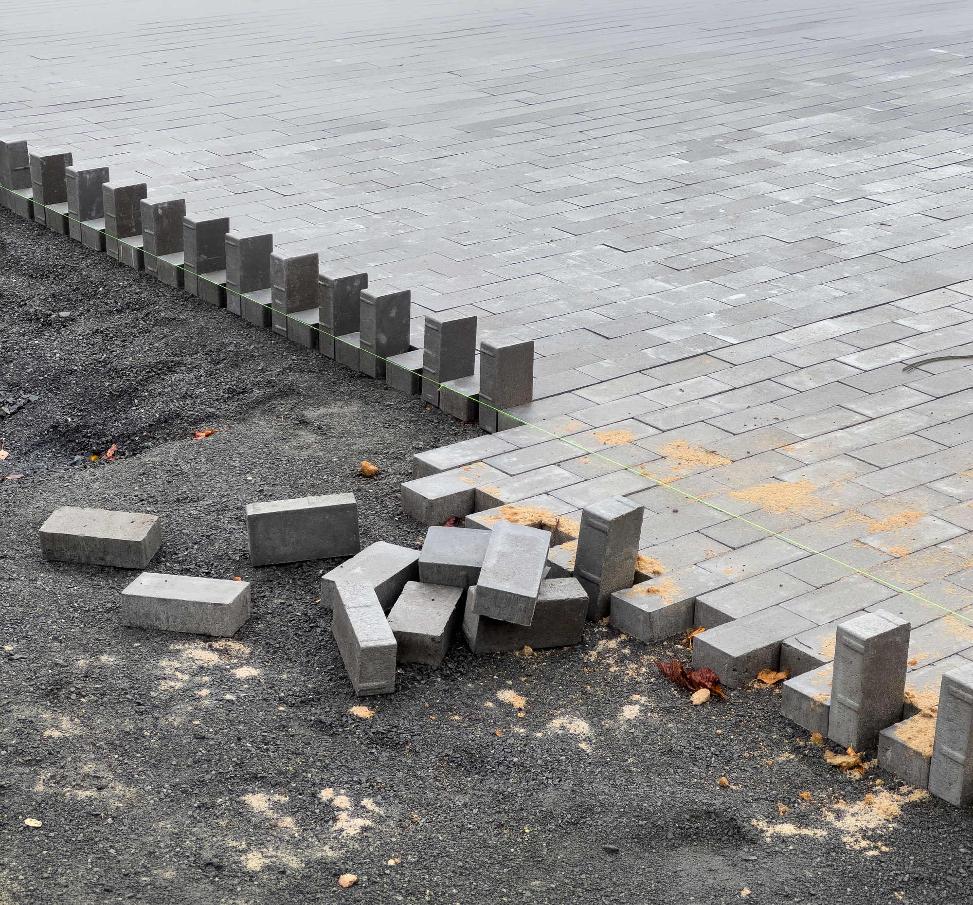 A crew is laying down paving stones to repair a section of pavement. The stones are gray and rectangular, and they are being laid in a pattern. The area around the stones is covered in gravel