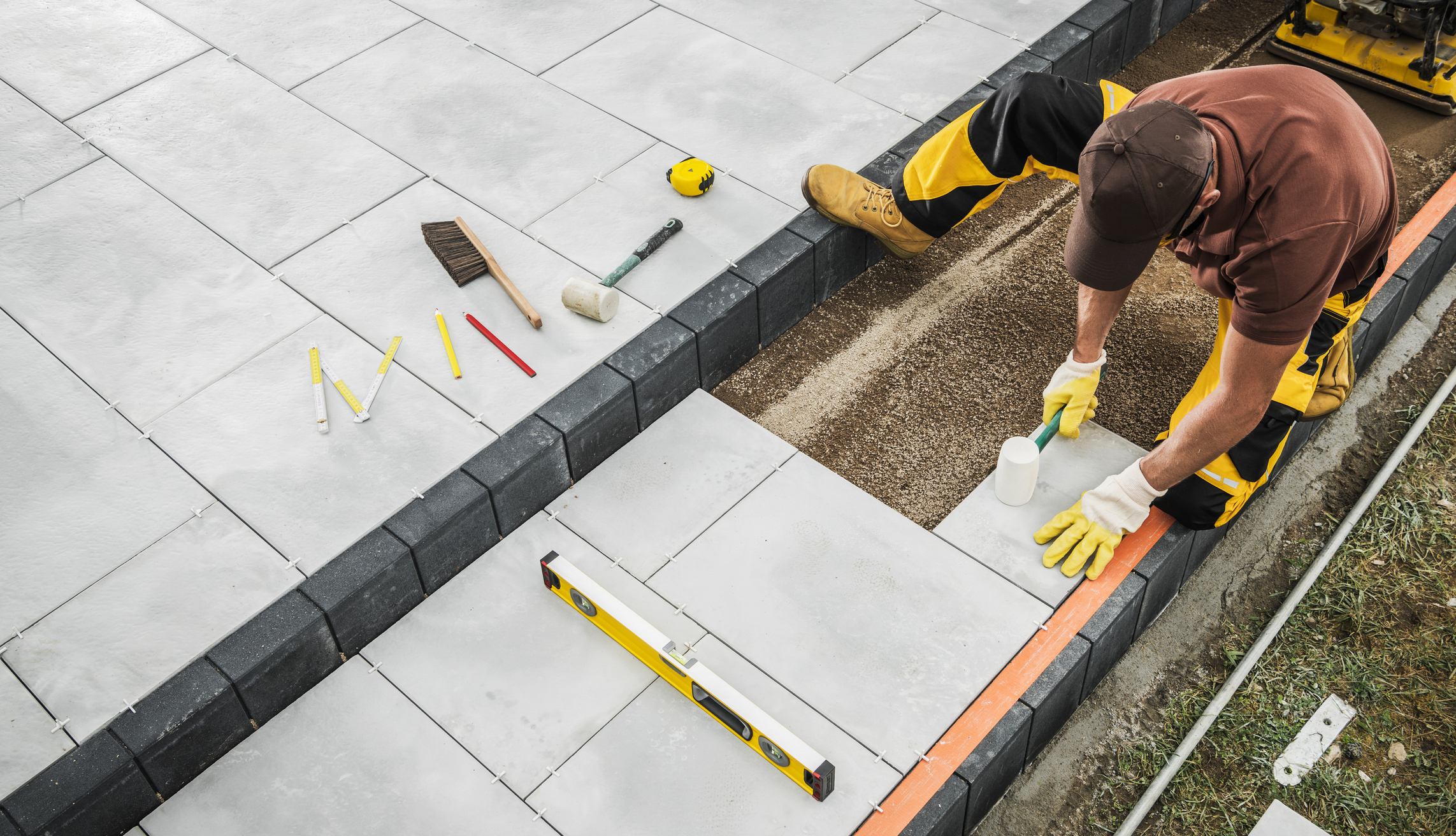 Professional Contractor Laying Pavers on a Patio With Tools at a Residential Backyard Site